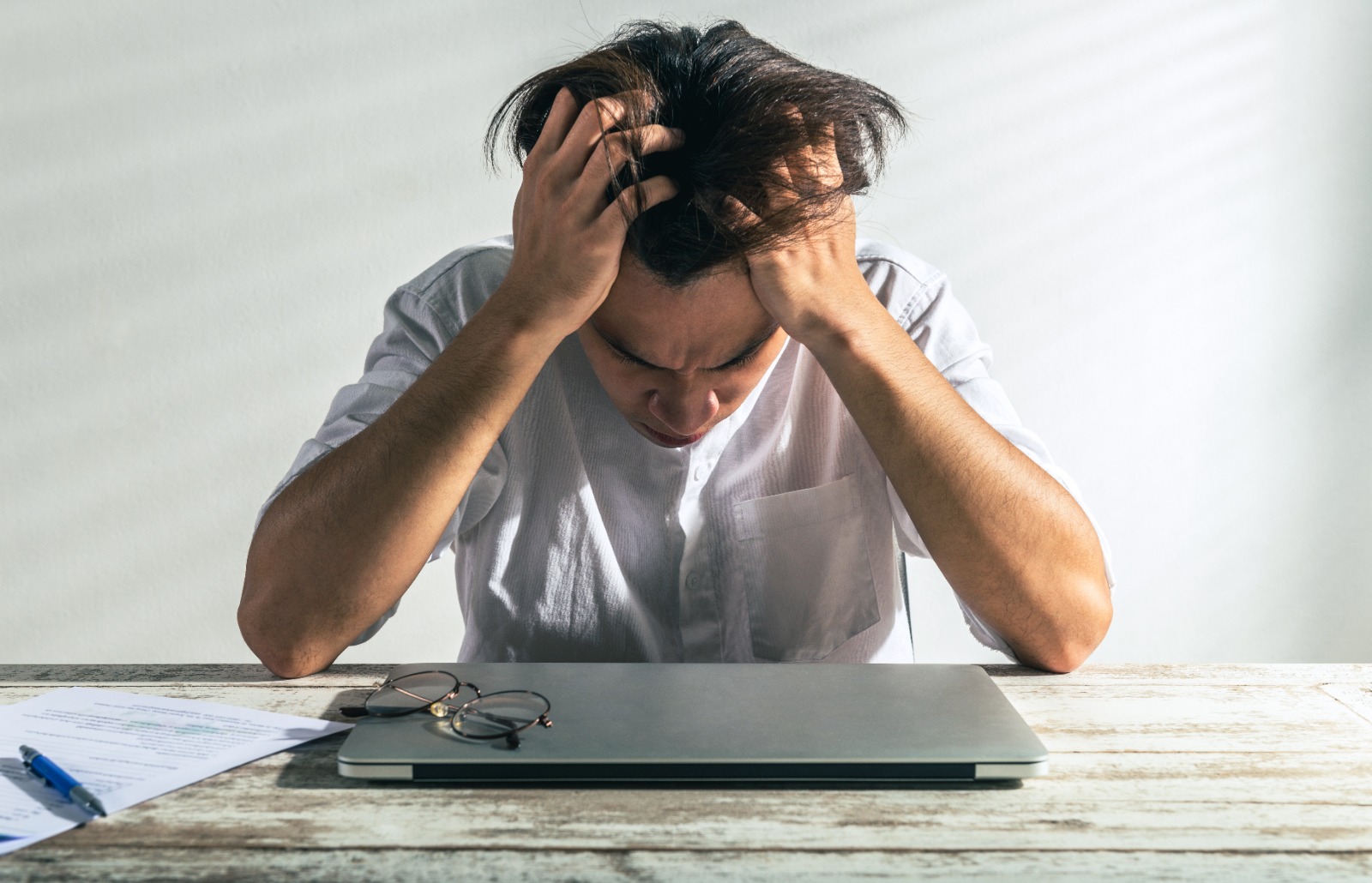 Financially stressed man with existing multiple loans from a money lender holding his head in hands in frustration